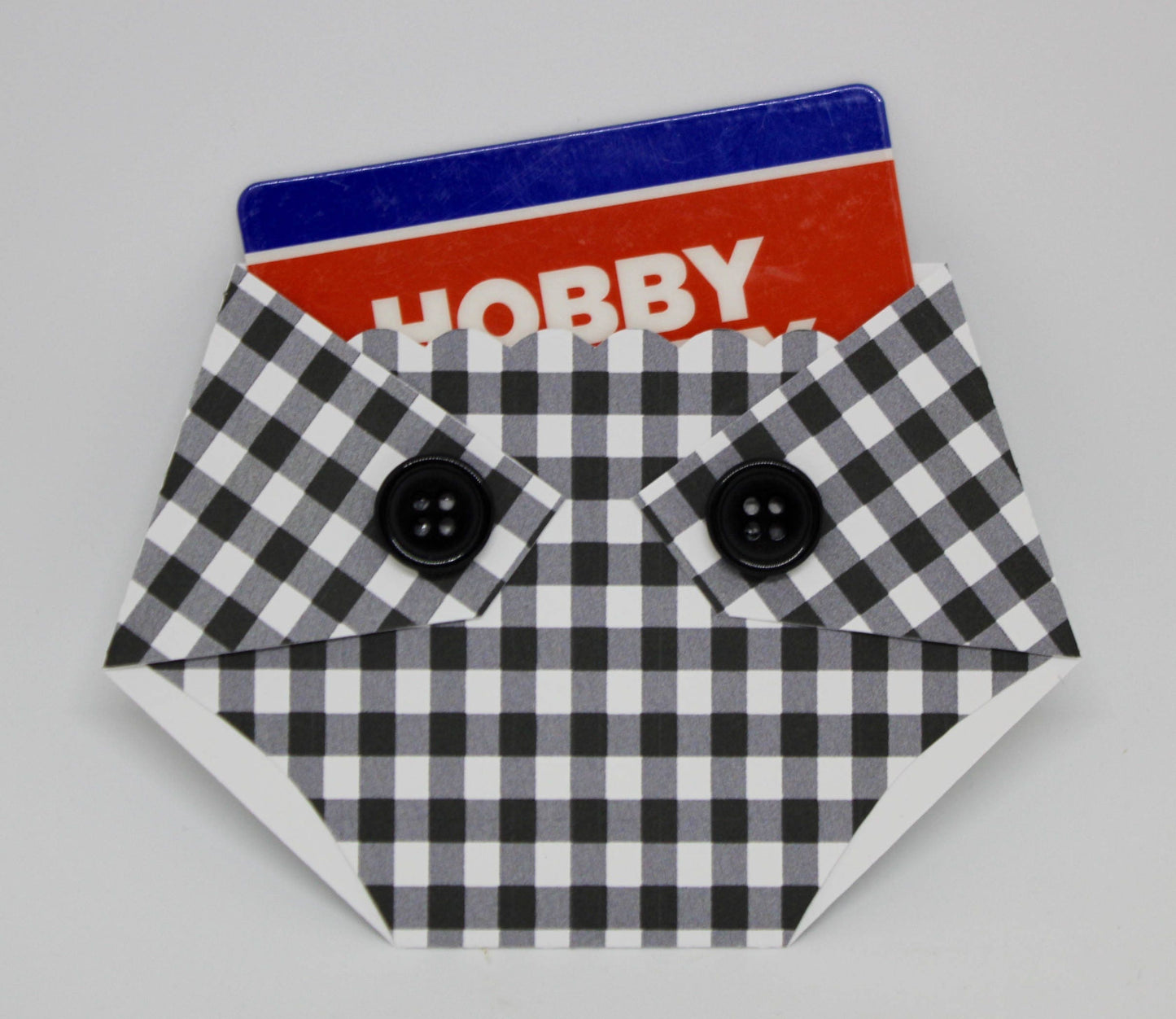 A plaid-patterned, diaper-shaped gift card holder with a black and white checkered design and black buttons, designed to hold a standard gift card.