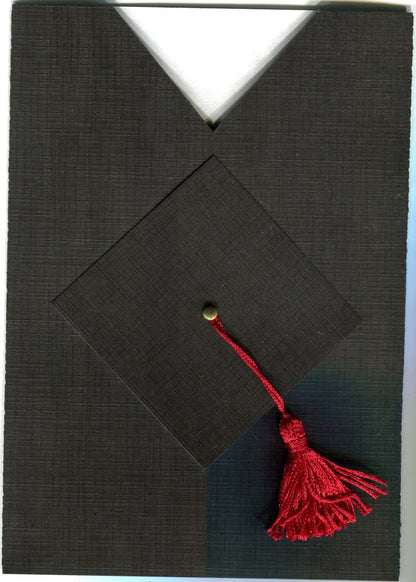 A folded black graduation invitation with a cap and gown design, featuring a red tassel and a gold brad