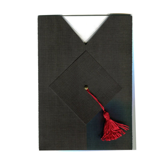 A folded black graduation invitation with a cap and gown design, featuring a red tassel and a gold brad,  with a white envelope.