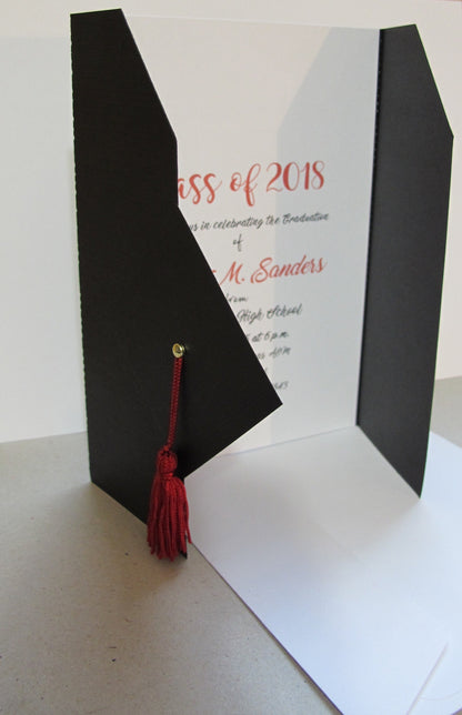 Side view folded open black graduation invitation with a cap and gown design, featuring a red tassel and a gold brad