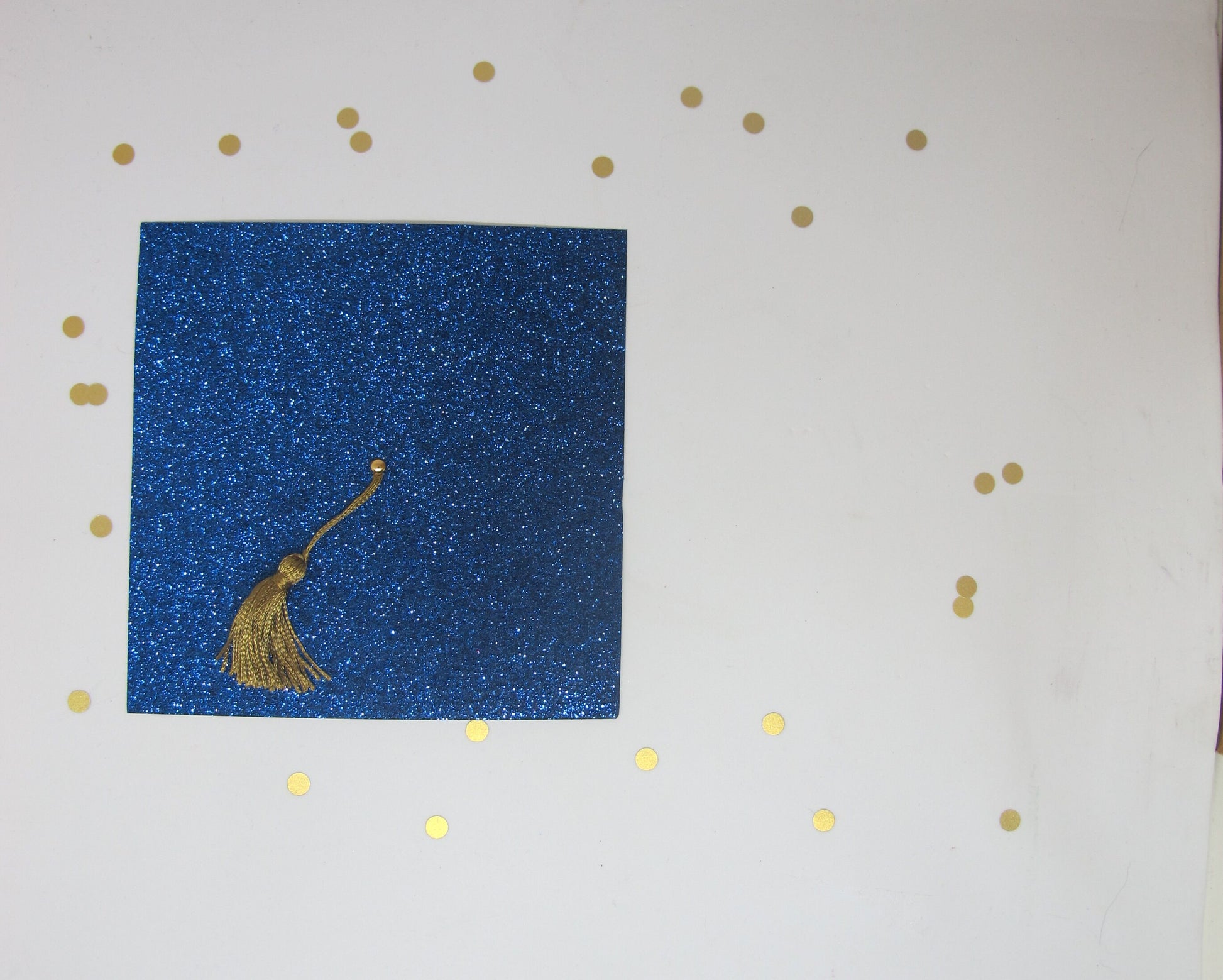 A blue glitter graduation cap invitation with a real gold tassel on a white background